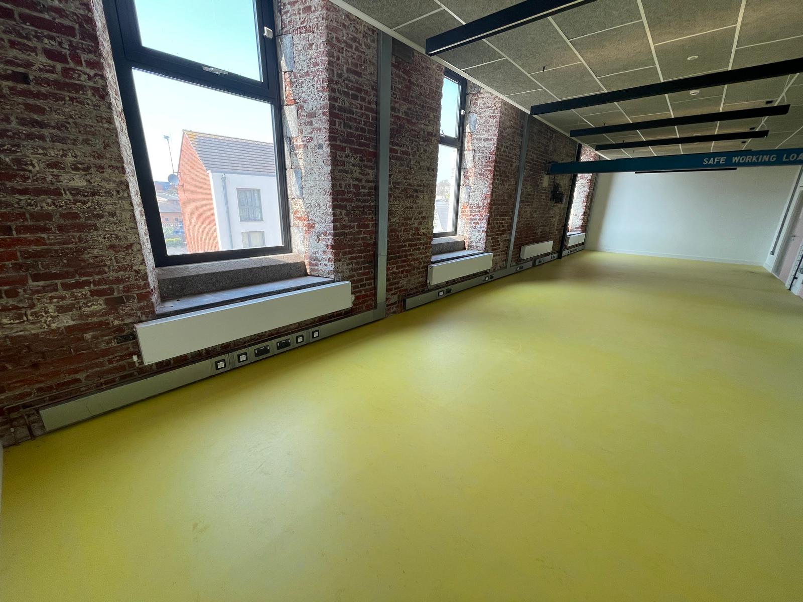 Commercial space with yellow-green Forbo Marmoleum flooring and exposed brick walls