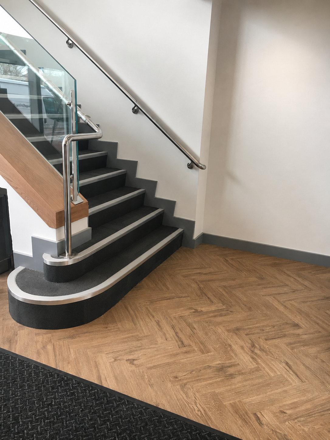Staircase with dark carpet, stair nosings and herringbone LVT landing