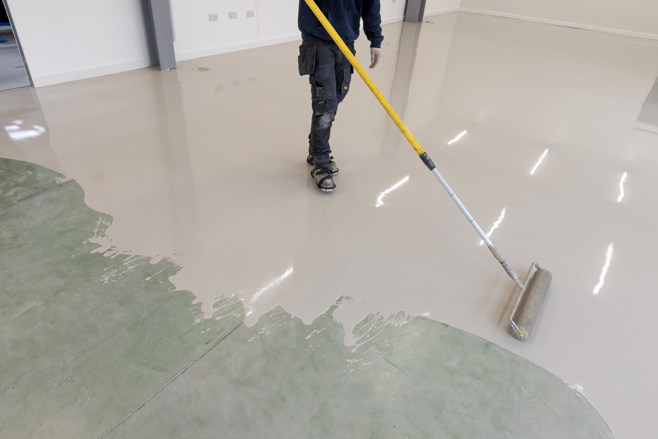 Installer spreading self-levelling smoothing compound across a large floor