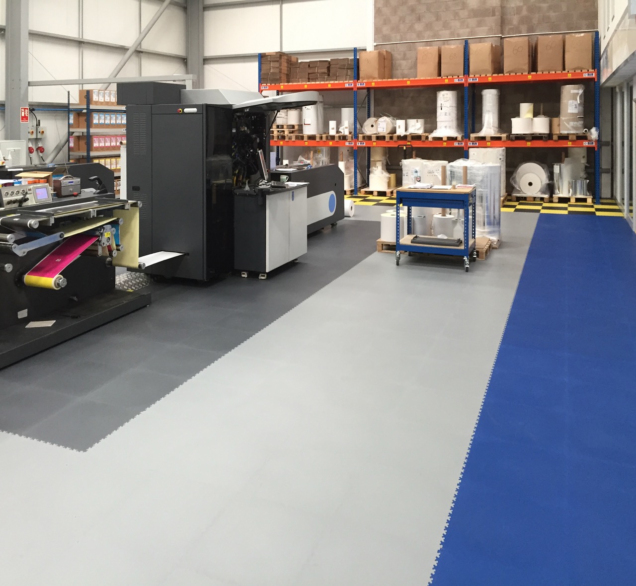 Industrial print workshop with grey interlocking floor tiles and a blue walkway