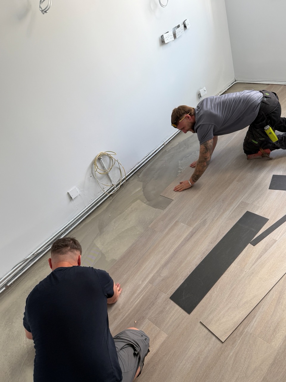 Two fitters installing wood-effect LVT planks in a room