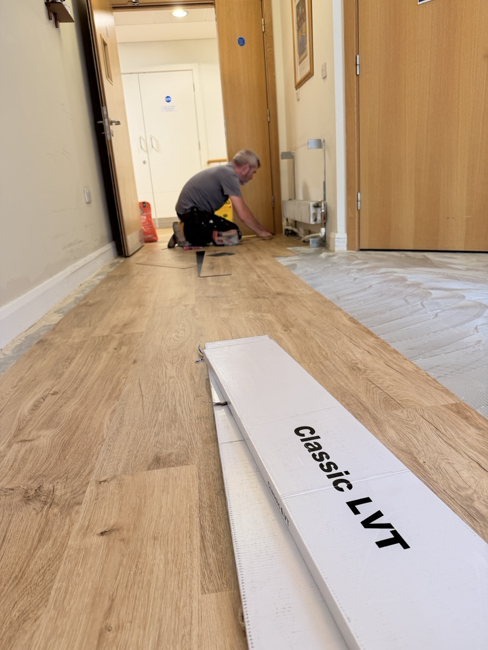 Fitter installing oak-effect LVT planks along a corridor